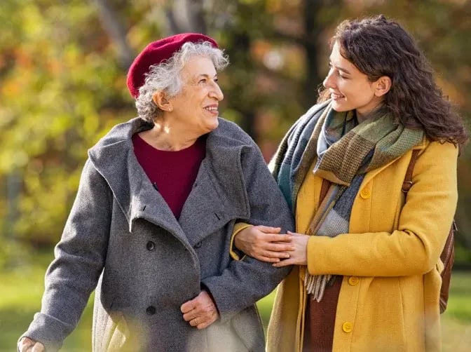 2 women - old and young - go for a walk together and smile at each other as a symbol of quality of life in old age