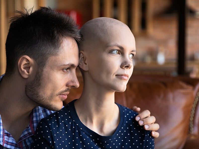 Woman with cancer looks out of the window with her husband