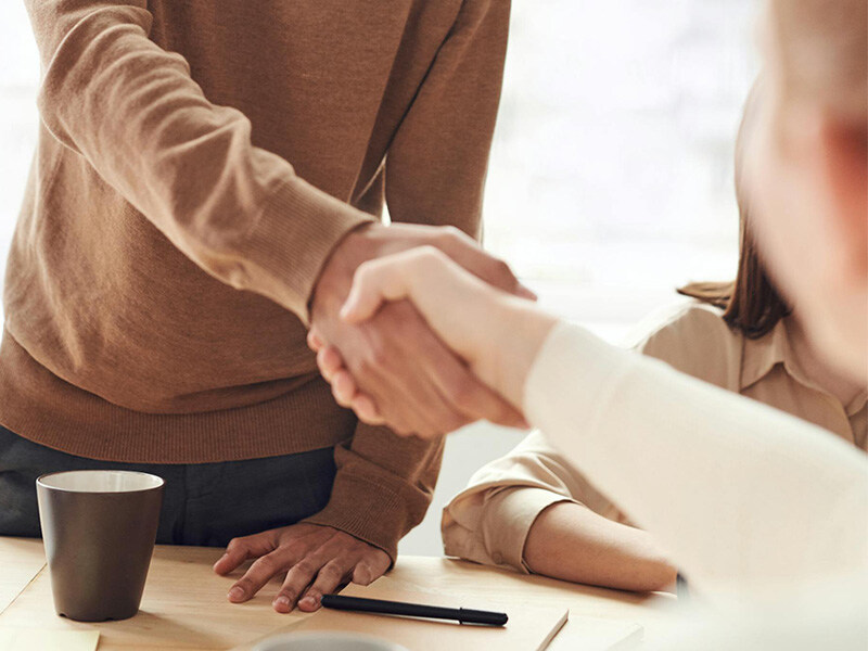 Two people shake hands in an office across a table, symbolizing fairness and professional cooperation.