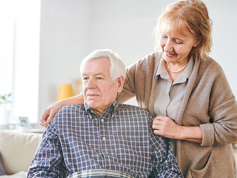 Woman adjusts the shirt of her husband, who is presumably in a wheelchair