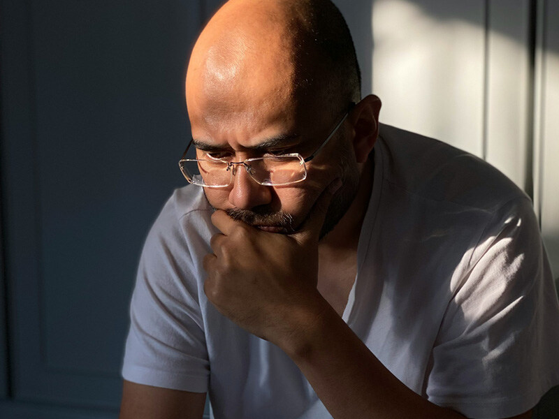 Thoughtful middle-aged man with glasses in a room flooded with sunlight, symbolizing reflection and concern for mental health.