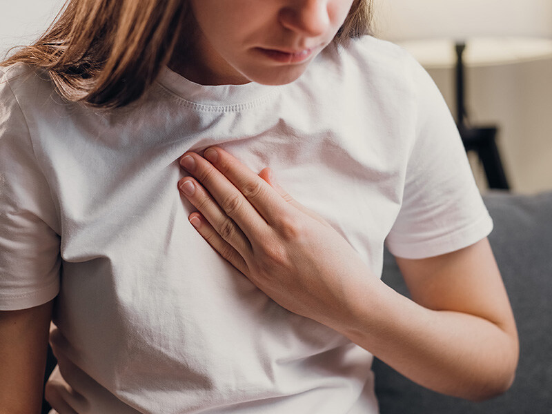 ne person holds their chest, dressed in a simple white T-shirt, symbolizing long Covid complaints.