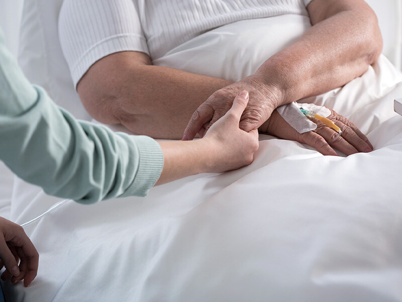 A person comfortingly holds the hand of an elderly person with an IV access in bed, symbolizing private Spitex services in the home environment.