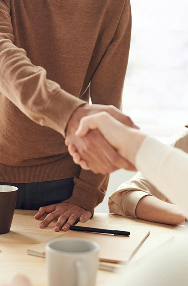 Two people shake hands in an office across a table, symbolizing fairness and professional cooperation.