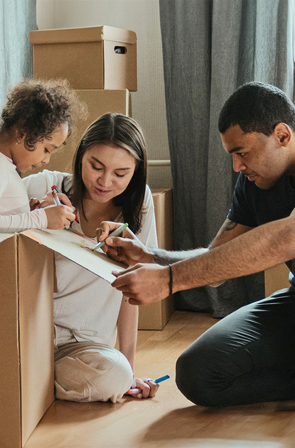 A happy family painting and playing on the floor, surrounded by moving boxes.