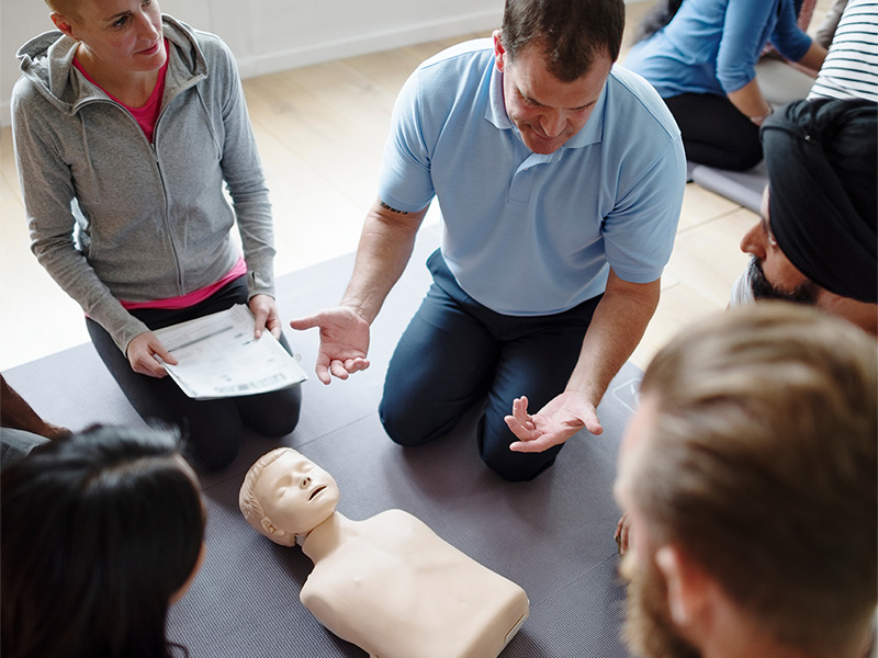 A first aid course for family caregivers who watch an instructor demonstrate the use of CPR on a training manikin.